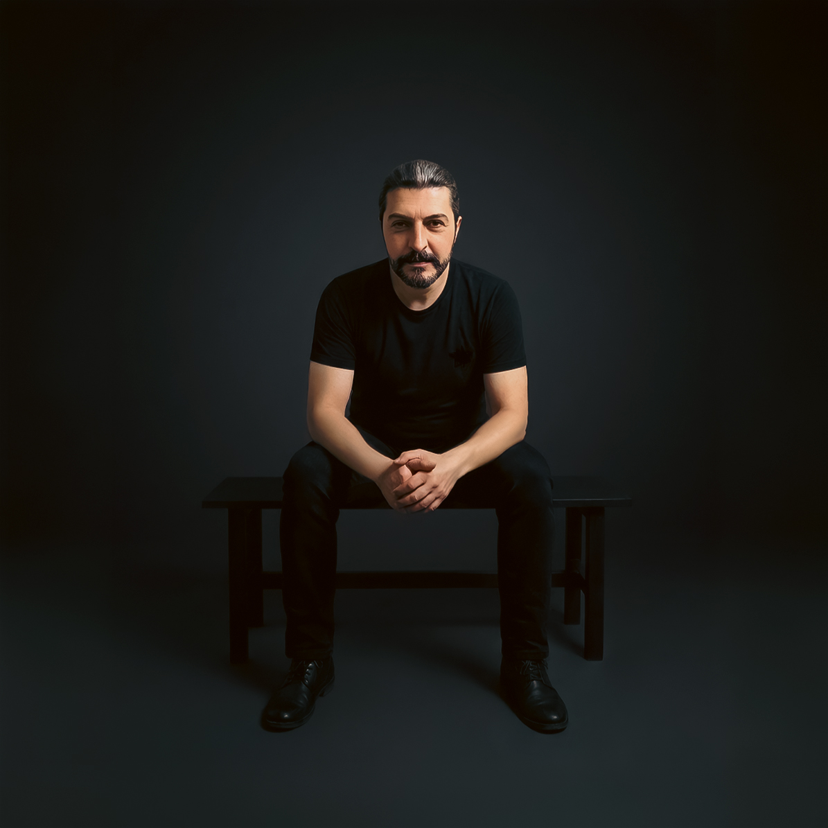 Murat Saatci sitting on a bench in a dark studio